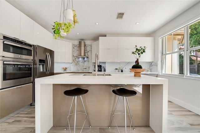 kitchen featuring wall chimney exhaust hood, modern cabinets, visible vents, and appliances with stainless steel finishes