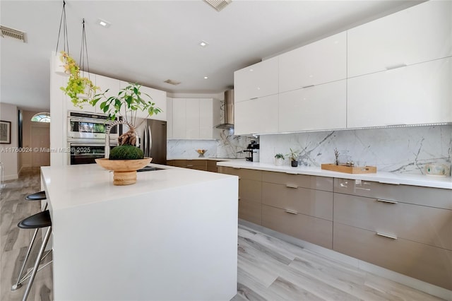 kitchen with a breakfast bar, stainless steel appliances, decorative backsplash, wall chimney exhaust hood, and modern cabinets