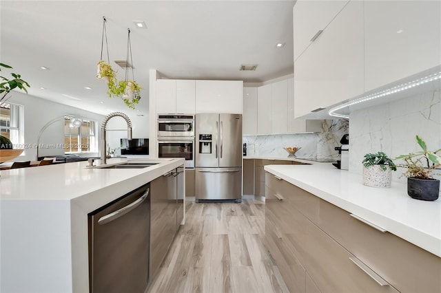 kitchen with a sink, stainless steel appliances, light countertops, modern cabinets, and backsplash
