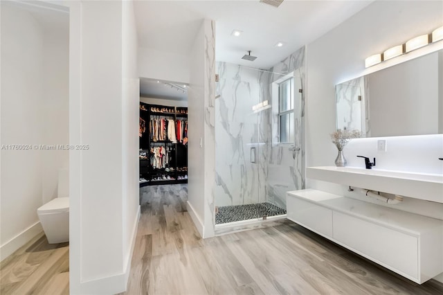 bathroom featuring vanity, wood finished floors, baseboards, and a marble finish shower