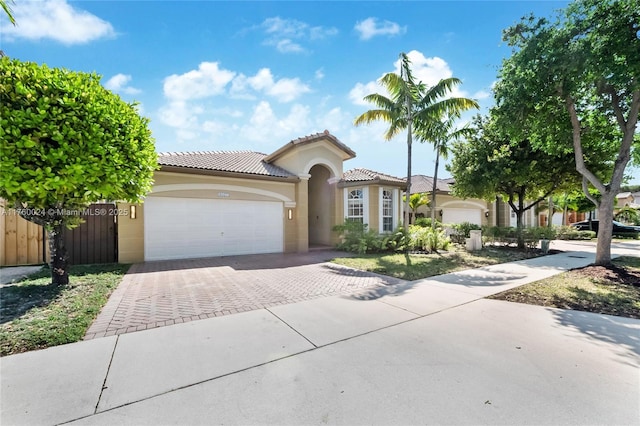 mediterranean / spanish house with stucco siding, driveway, fence, an attached garage, and a tiled roof