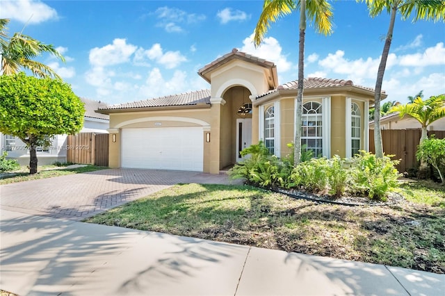 mediterranean / spanish-style home with an attached garage, a tile roof, decorative driveway, and fence