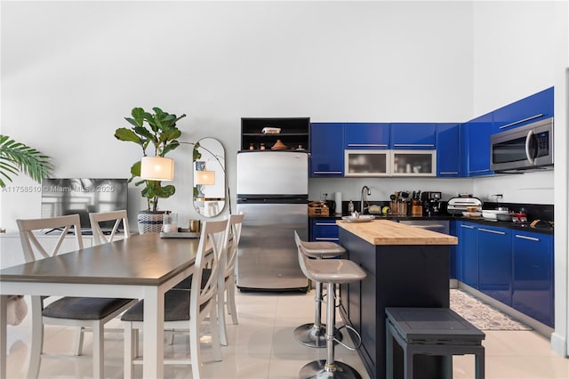 kitchen featuring blue cabinetry, a center island, appliances with stainless steel finishes, a breakfast bar area, and butcher block counters