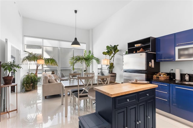 kitchen featuring blue cabinetry, a sink, butcher block counters, and freestanding refrigerator