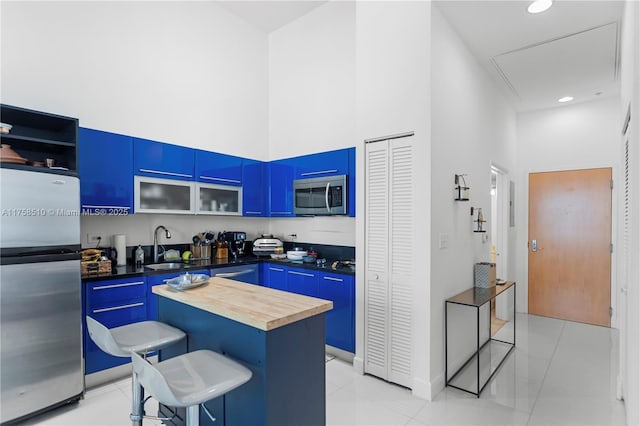 kitchen featuring a kitchen bar, blue cabinets, appliances with stainless steel finishes, and a towering ceiling