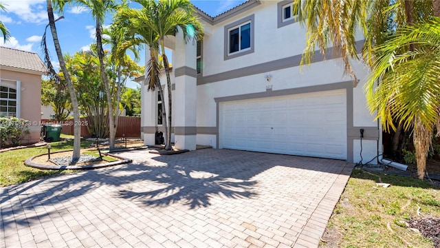 view of front of property with fence, an attached garage, stucco siding, a tiled roof, and decorative driveway