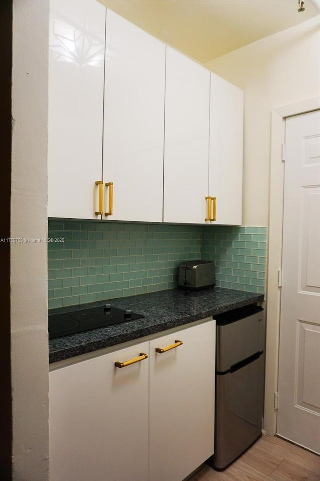 kitchen with light wood-type flooring, tasteful backsplash, refrigerator, white cabinetry, and black electric cooktop