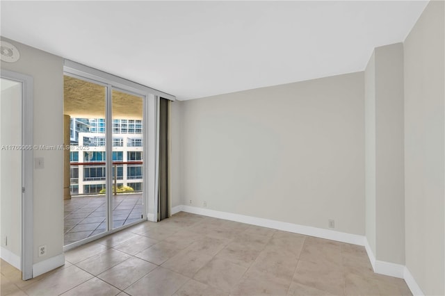 tiled empty room featuring floor to ceiling windows and baseboards