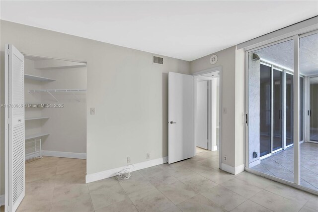 unfurnished bedroom with access to exterior, visible vents, baseboards, a wall of windows, and light tile patterned floors