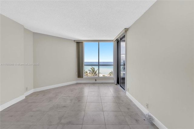 unfurnished room with baseboards, a water view, and a textured ceiling