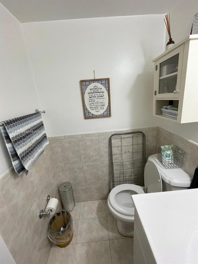 half bath featuring tile patterned floors, wainscoting, toilet, and tile walls