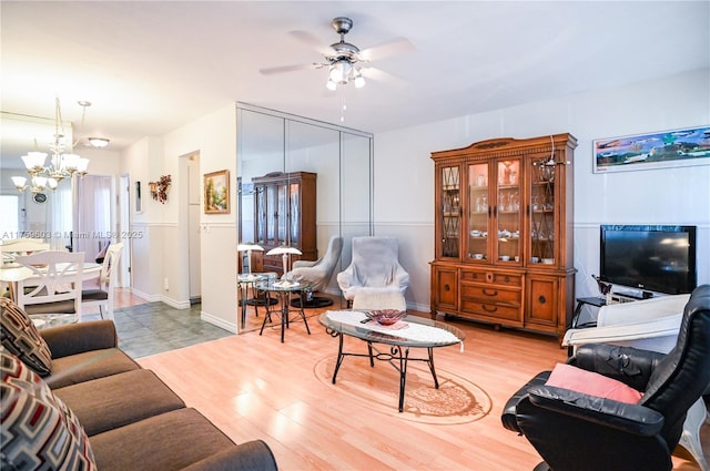 living room with light wood-style flooring, ceiling fan with notable chandelier, and baseboards