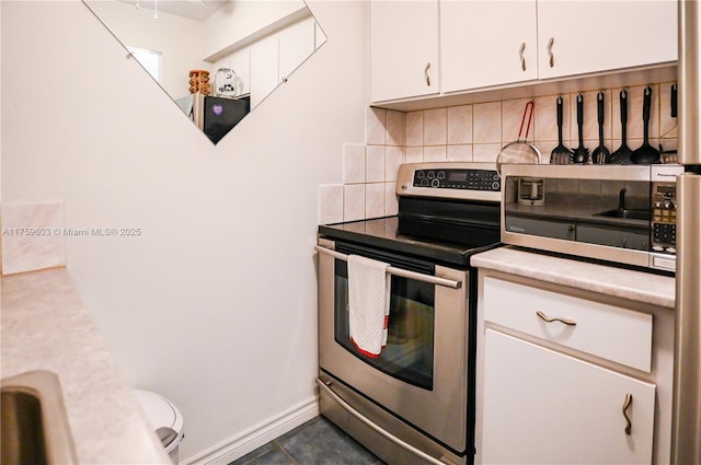 kitchen featuring baseboards, light countertops, decorative backsplash, stainless steel range with electric stovetop, and white cabinetry