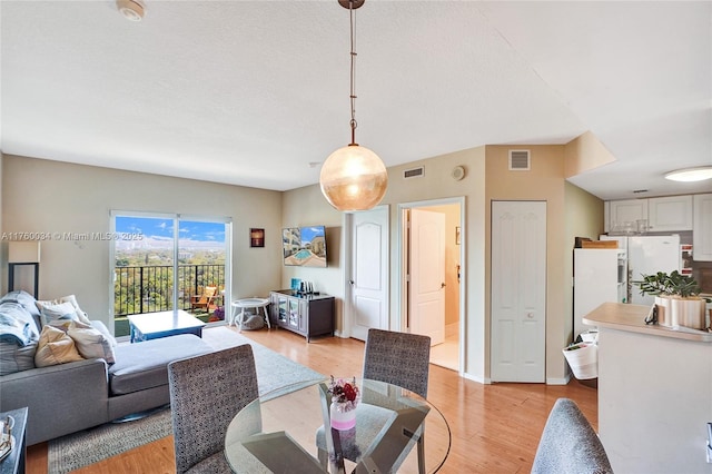 living area with light wood finished floors, visible vents, a textured ceiling, and baseboards