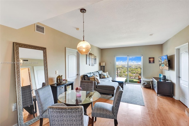 dining area featuring visible vents, light wood-style floors, and a textured ceiling