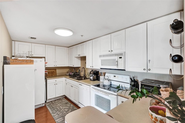 kitchen with visible vents, a sink, wood finished floors, white appliances, and white cabinets