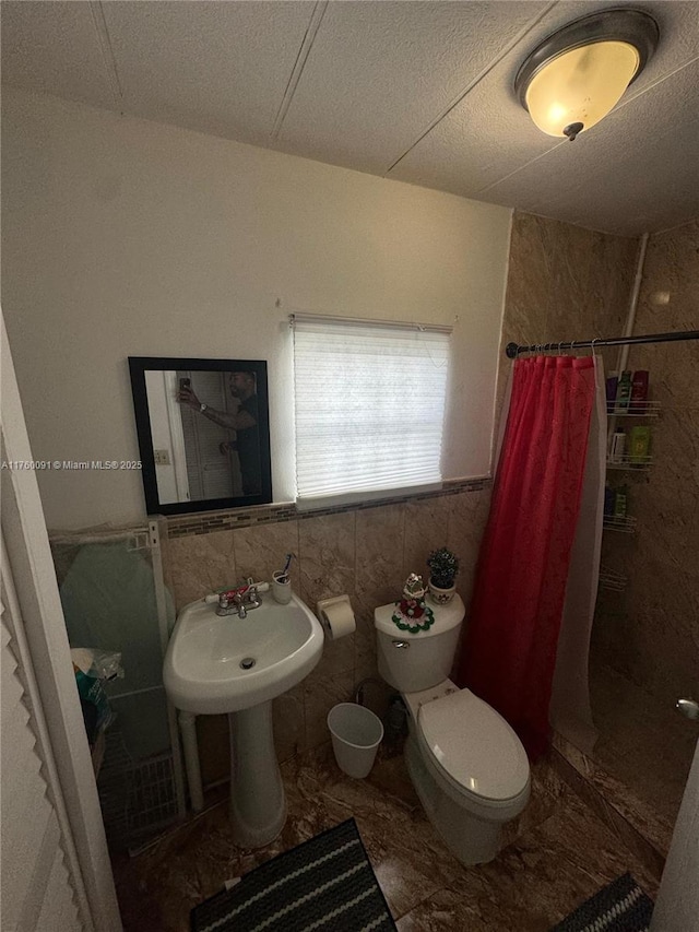 bathroom featuring a wainscoted wall, a shower with curtain, tile walls, and toilet