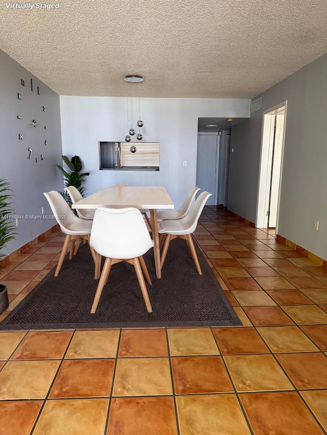 tiled dining space featuring visible vents, baseboards, and a textured ceiling