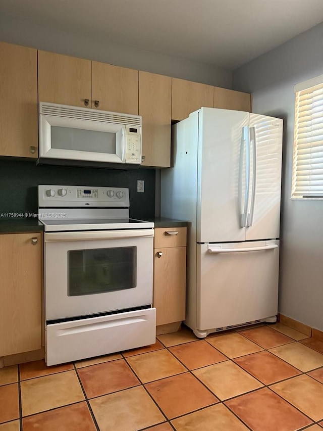 kitchen featuring white appliances, dark countertops, and light tile patterned flooring