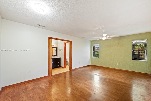 empty room featuring light wood-type flooring, visible vents, plenty of natural light, and a textured ceiling