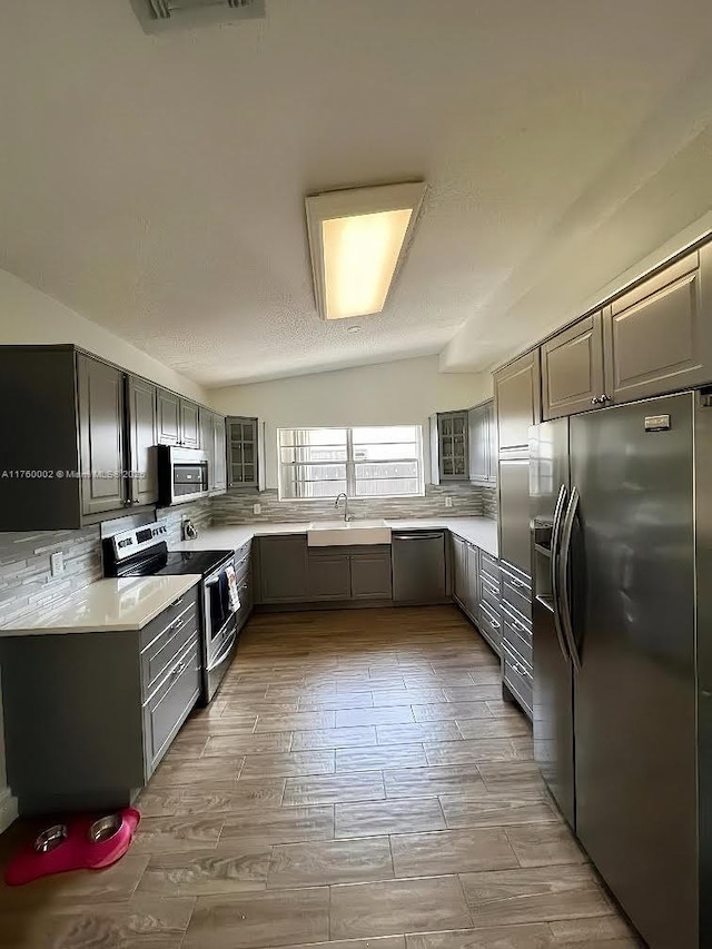 kitchen with gray cabinets, a sink, light countertops, appliances with stainless steel finishes, and tasteful backsplash