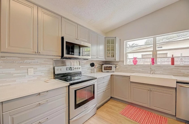 kitchen with light wood-style flooring, a sink, decorative backsplash, vaulted ceiling, and appliances with stainless steel finishes