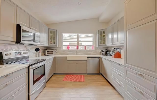 kitchen with a sink, tasteful backsplash, appliances with stainless steel finishes, glass insert cabinets, and vaulted ceiling