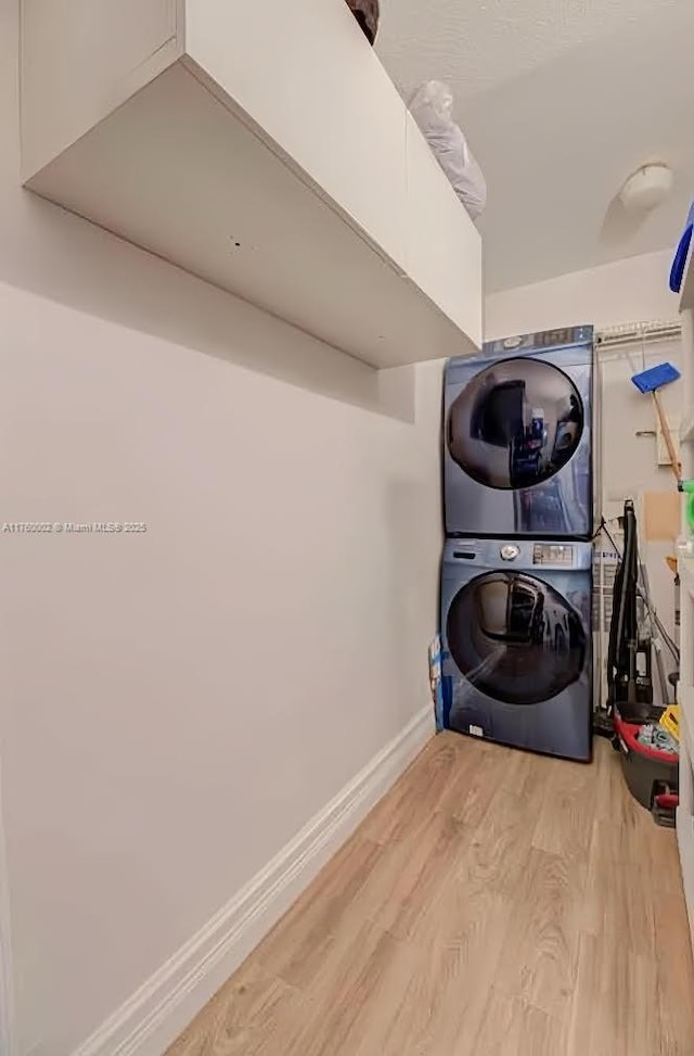 laundry room featuring baseboards, light wood-style flooring, laundry area, and stacked washing maching and dryer