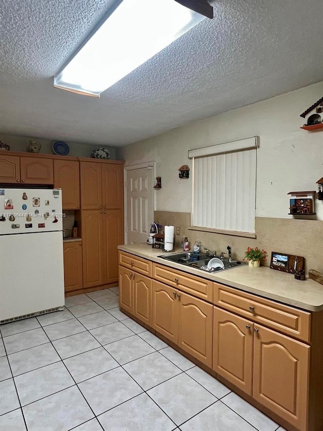 kitchen with light countertops, freestanding refrigerator, light tile patterned flooring, a textured ceiling, and a sink