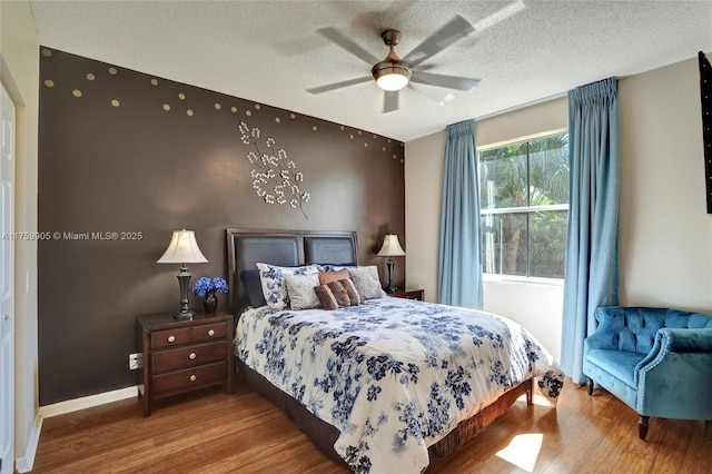 bedroom featuring ceiling fan, baseboards, a textured ceiling, and wood finished floors