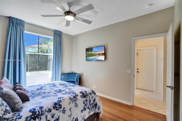 bedroom with ceiling fan, a textured ceiling, baseboards, and wood finished floors