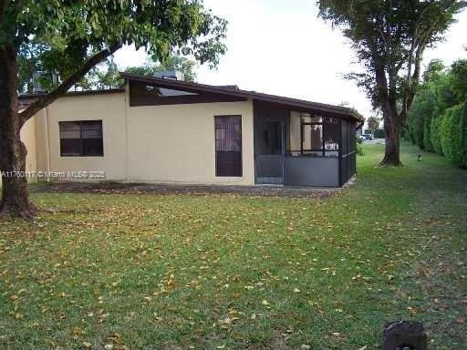 view of property exterior with stucco siding, a lawn, and a sunroom