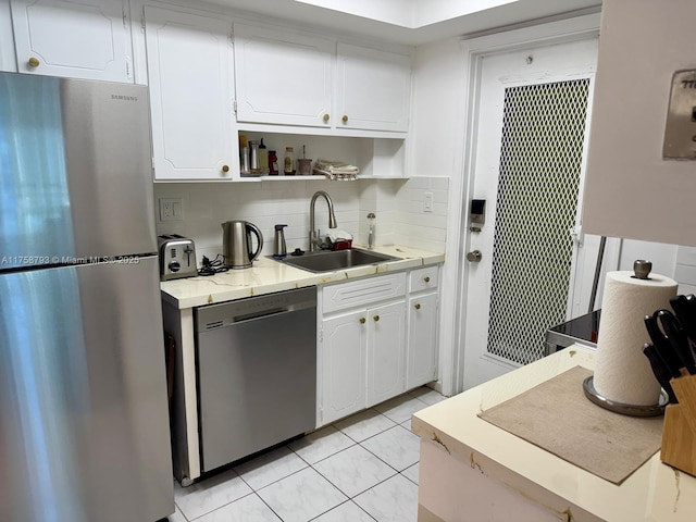 kitchen with backsplash, light tile patterned floors, appliances with stainless steel finishes, white cabinets, and a sink