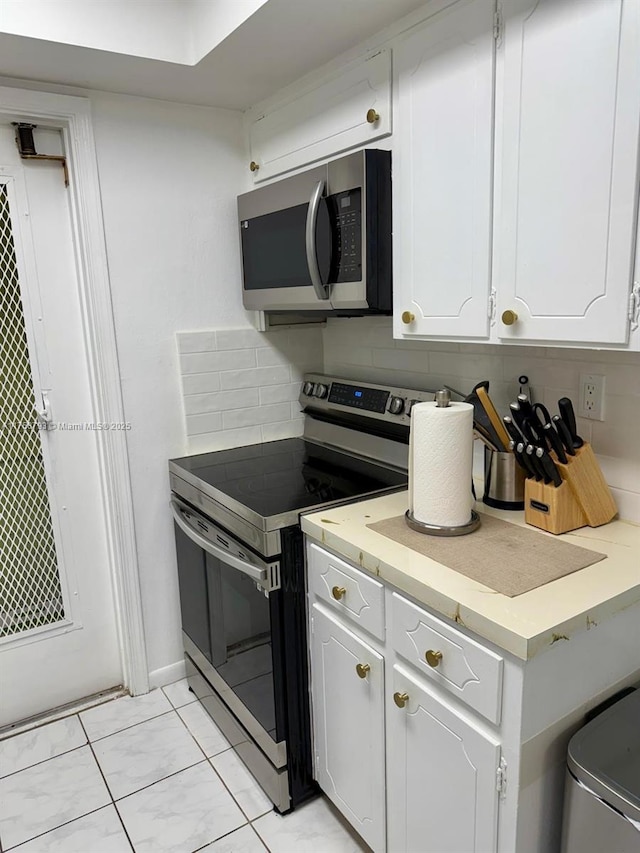 kitchen with tasteful backsplash, white cabinets, appliances with stainless steel finishes, and light countertops