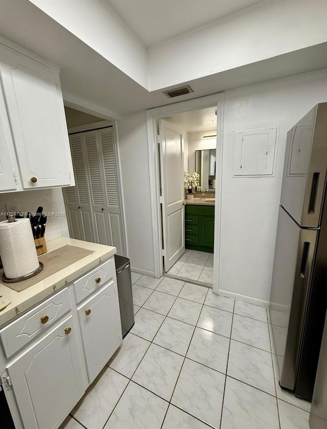 kitchen with visible vents, light countertops, freestanding refrigerator, marble finish floor, and white cabinetry