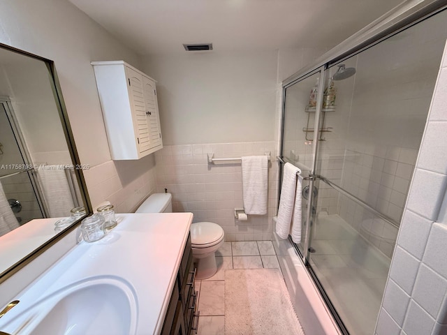 bathroom featuring visible vents, a shower stall, toilet, vanity, and tile walls