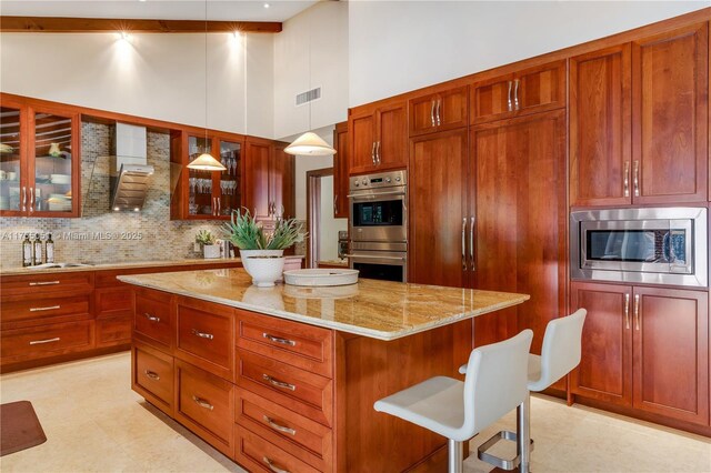 5780 Magnolia Ln, Coral Gables, FL 33156 - kitchen with stainless steel appliances, wall chimney exhaust hood, a high ceiling, tasteful backsplash, and a kitchen breakfast bar