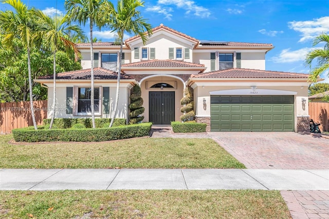 mediterranean / spanish home featuring fence, solar panels, stucco siding, a garage, and decorative driveway