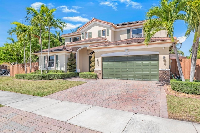 mediterranean / spanish-style house with stucco siding, decorative driveway, roof mounted solar panels, fence, and a garage