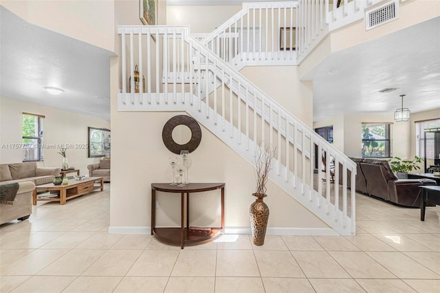 staircase featuring tile patterned floors, visible vents, a high ceiling, and baseboards