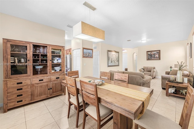 dining space featuring light tile patterned flooring, visible vents, arched walkways, and baseboards
