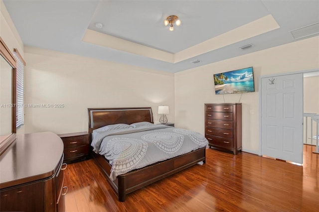 bedroom featuring a tray ceiling, visible vents, and wood finished floors