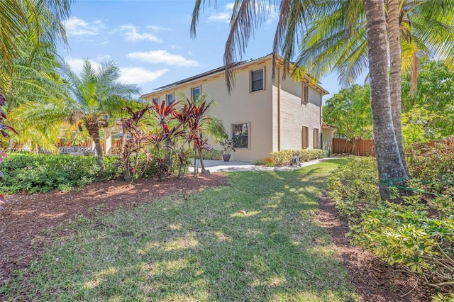 view of side of home with a patio area, stucco siding, a lawn, and fence
