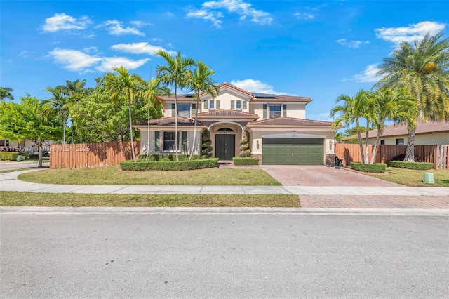 mediterranean / spanish-style home featuring stucco siding, a tile roof, decorative driveway, roof mounted solar panels, and fence