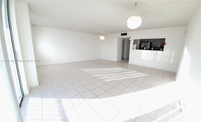 spare room with light tile patterned floors, visible vents, a textured ceiling, and baseboards