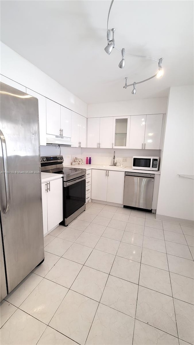 kitchen with a sink, light countertops, white cabinets, under cabinet range hood, and appliances with stainless steel finishes