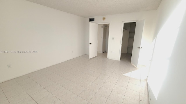 unfurnished bedroom with visible vents, a walk in closet, light tile patterned floors, a closet, and a textured ceiling