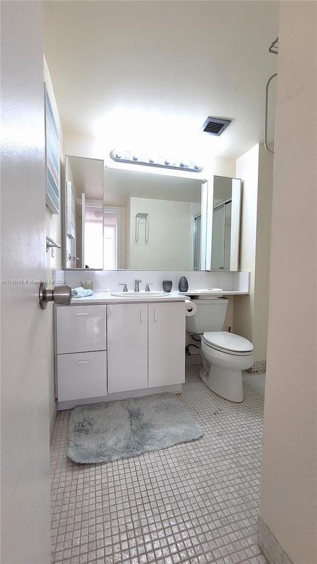 bathroom featuring vanity, a shower with shower door, visible vents, tile patterned floors, and toilet