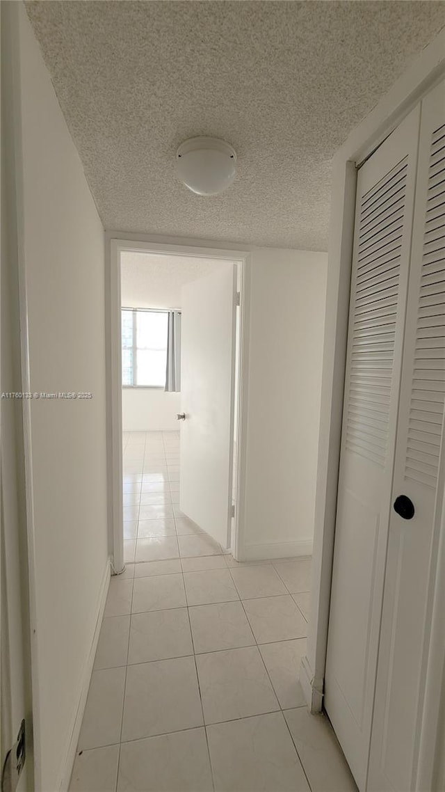 hall featuring light tile patterned floors, baseboards, and a textured ceiling