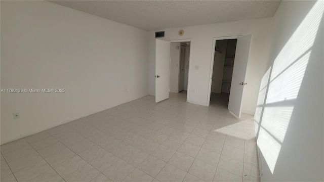 unfurnished bedroom featuring visible vents, a walk in closet, light tile patterned flooring, a closet, and a textured ceiling